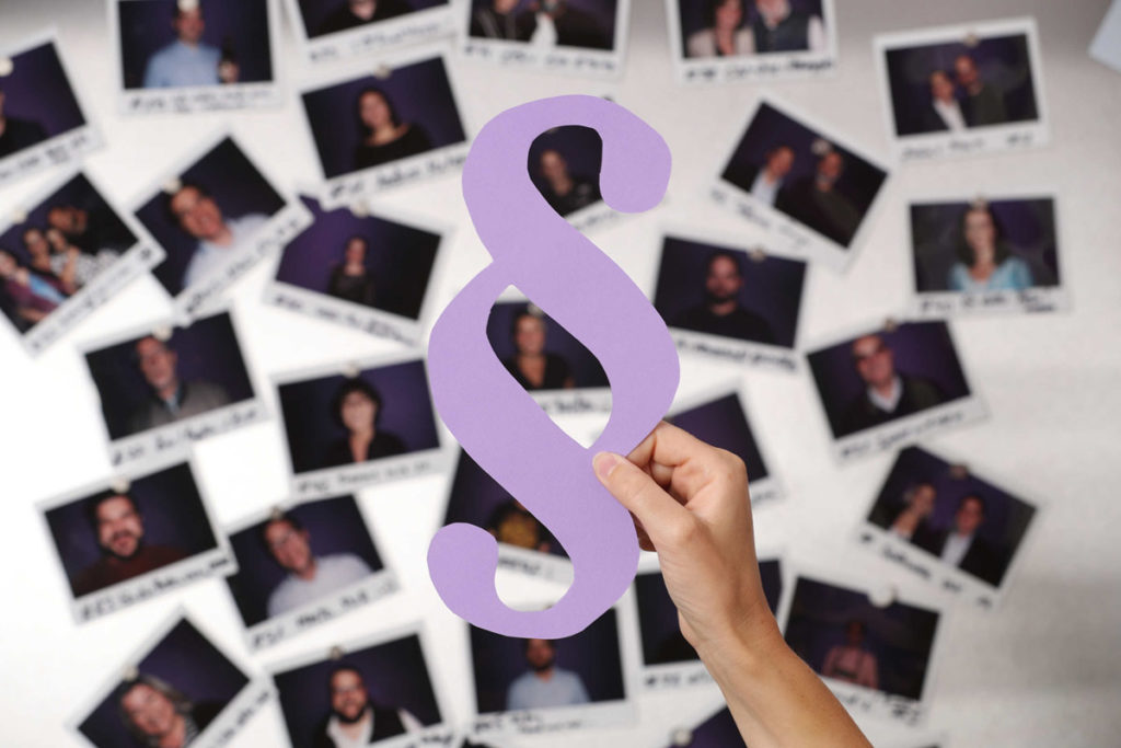 Lilafarbenes Paragrafen-Symbol vor einer Wand mit Polaroids, gibt einen Hinweis auf die Thematik Bildrechte